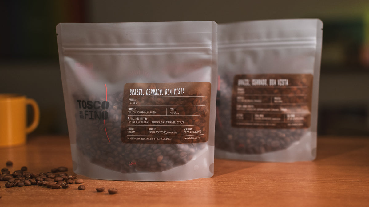 Two bags of Tosco Fino Brazil Cerrado Boa Vista specialty coffee on a wooden café table
