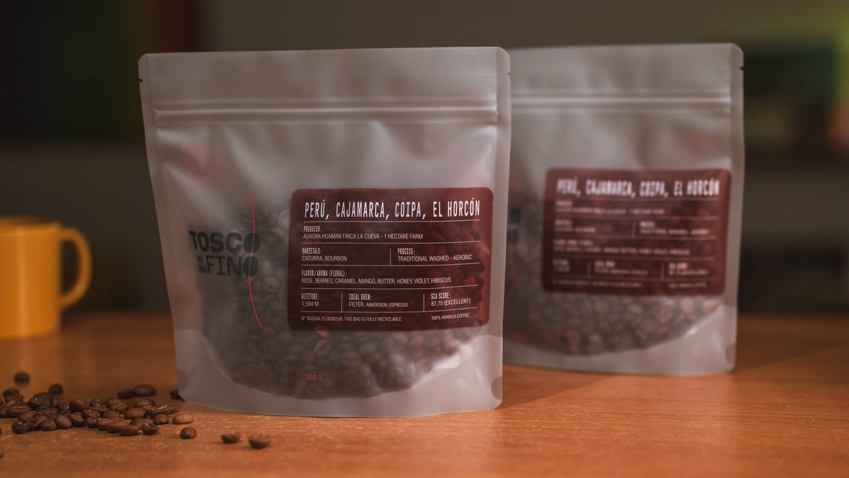 Two bags of Tosco Fino Peru Cajamarca specialty coffee on a wooden café table