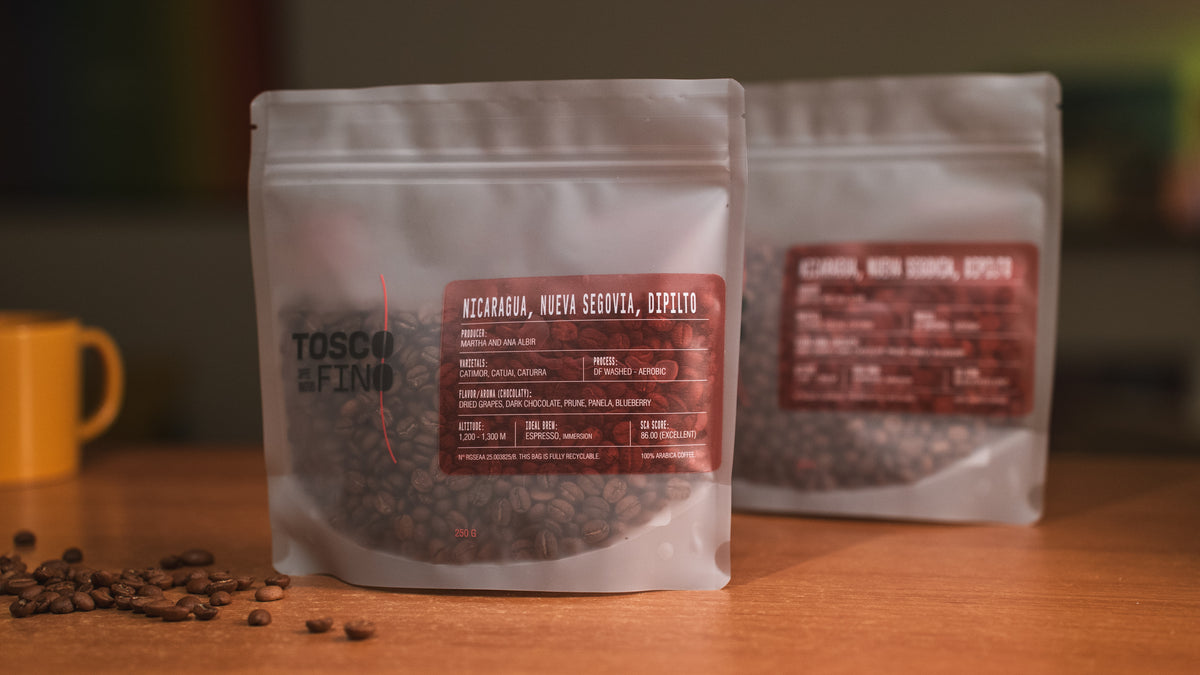 Two bags of Tosco Fino Nicaragua Nueva Segovia specialty coffee on a wooden café table